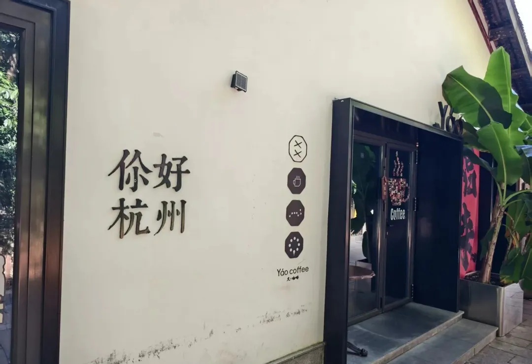 A quiet Hangzhou lane beside a white wall bearing a greeting to the city