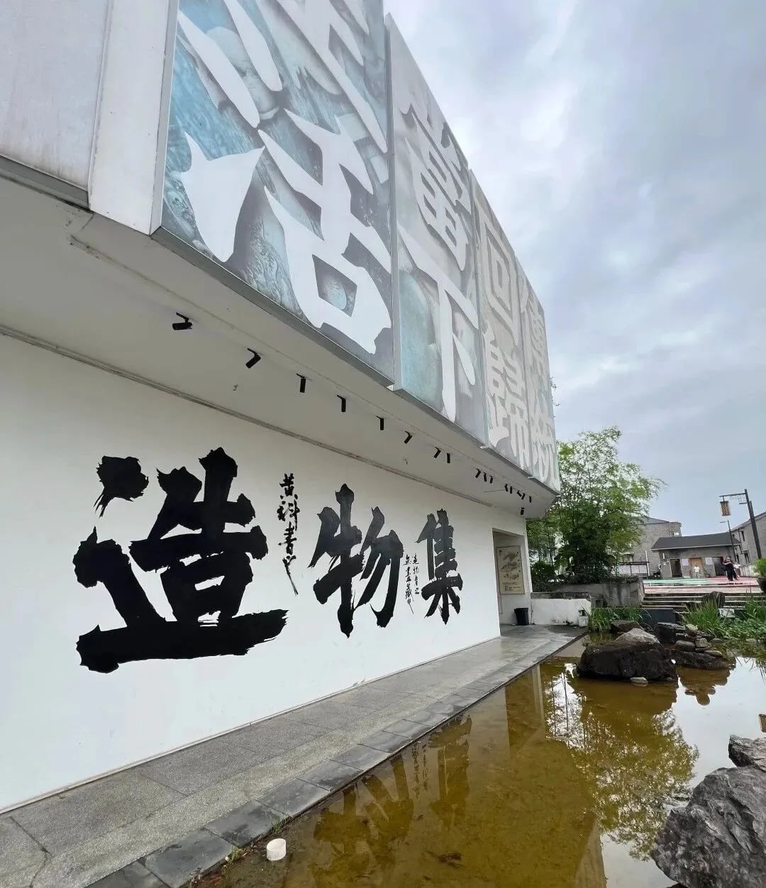 Ziran Zaowu lettering on a white exterior wall beside a shallow pool