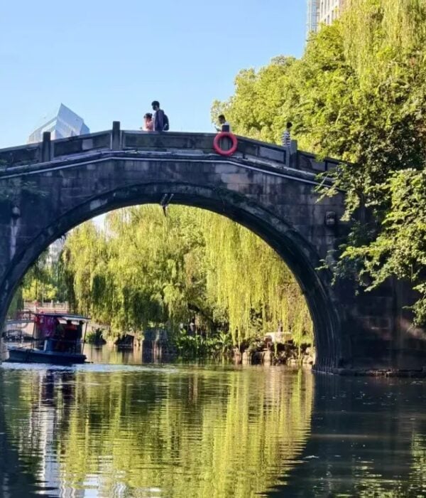 A traditional stone arch bridge with a small passenger boat on the Donghe River