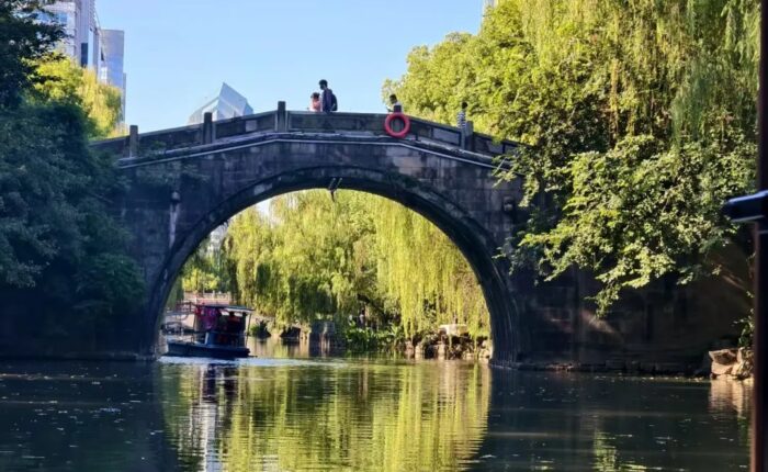 A traditional stone arch bridge with a small passenger boat on the Donghe River