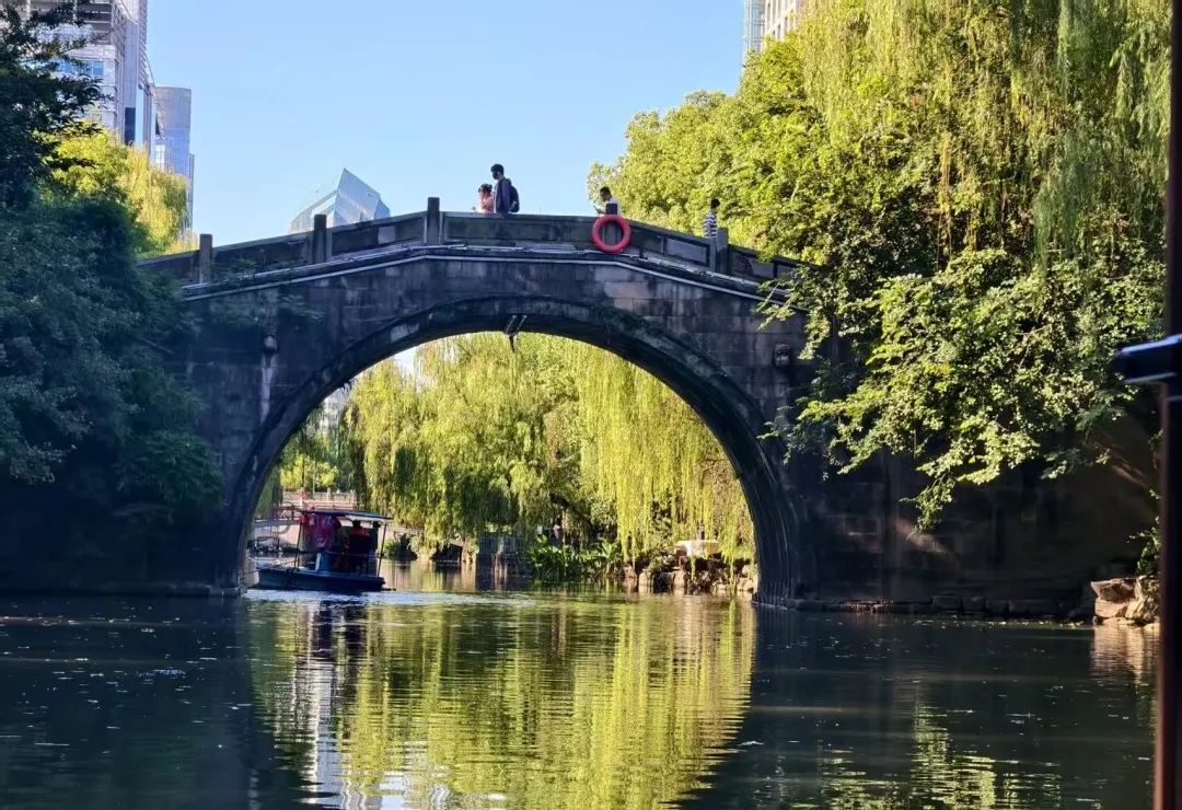 A traditional stone arch bridge with a small passenger boat on the Donghe River