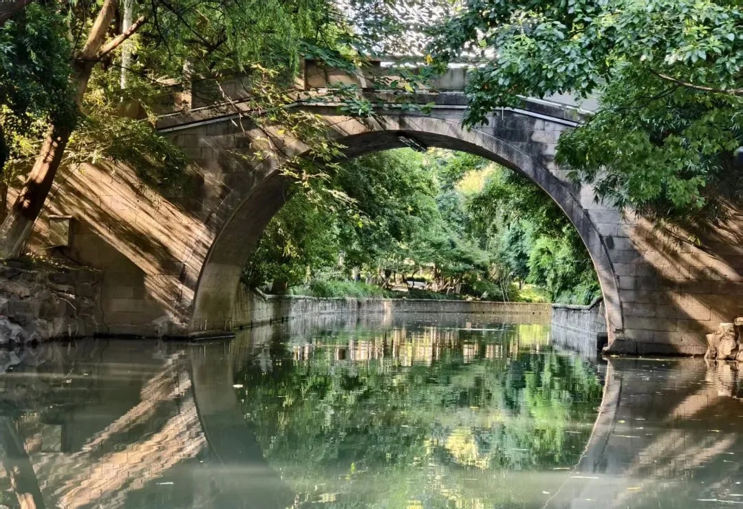 An old stone bridge framed by green trees along the Donghe River